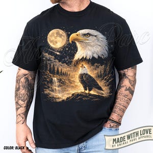 Może przedstawiać: Czarny t-shirt z szczeg&oacute;łową grafiką orła, księżyca w pełni, wodospadu i lasu. Orzeł jest przedstawiony w dw&oacute;ch pozach. Widoczny jest r&oacute;wnież tekst "MADE WITH LOVE BY ANIMAL PARC APPAREL".