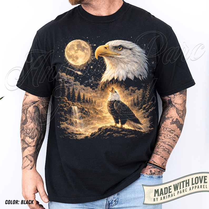 Może przedstawiać: Czarny t-shirt z szczeg&oacute;łową grafiką orła, księżyca w pełni, wodospadu i lasu. Orzeł jest przedstawiony w dw&oacute;ch pozach. Widoczny jest r&oacute;wnież tekst "MADE WITH LOVE BY ANIMAL PARC APPAREL".