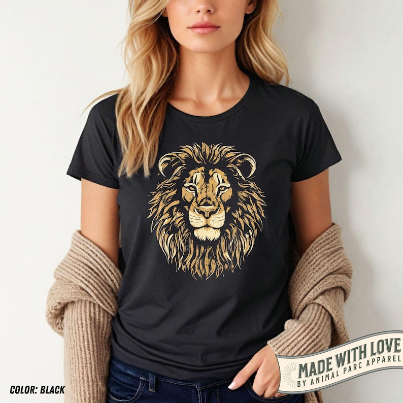 May include: Black t-shirt featuring a golden lion head design. The lion's mane is detailed with textured lines, and the shirt has a crew neck. The words 'MADE WITH LOVE BY ANIMAL PARC APPAREL' are printed on a white banner. The color is black.