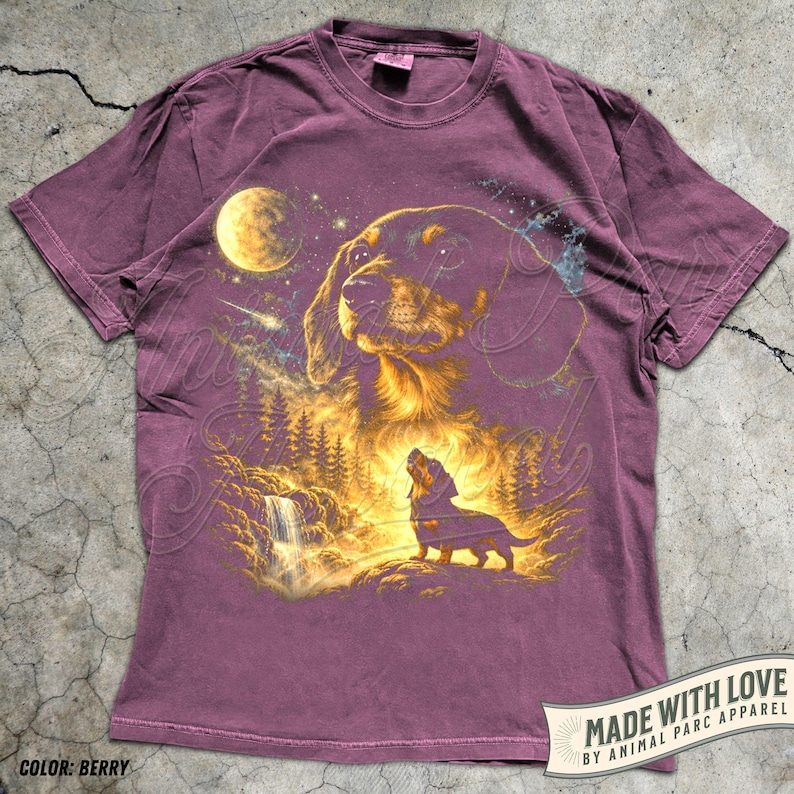 May include: Berry-colored t-shirt featuring a detailed illustration of a dachshund dog under a night sky with a full moon, waterfall, and forest. The design includes the text "MADE WITH LOVE BY ANIMAL PARC APPAREL" and "COLOR: BERRY".