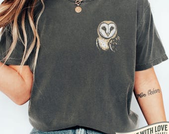 May include: Pepper-colored t-shirt featuring a detailed owl graphic on the chest. The shirt has a relaxed fit and short sleeves. The text "MADE WITH LOVE BY ANIMAL PARC APPAREL" is printed on a banner at the bottom.