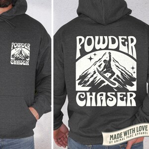 May include: Dark grey hoodie with a front pocket and hood. The front displays a white graphic with "POWDER CHASER" and a mountain scene. The back has a larger version of the same design, with a snowboarder. "MADE WITH LOVE" is printed at the bottom.