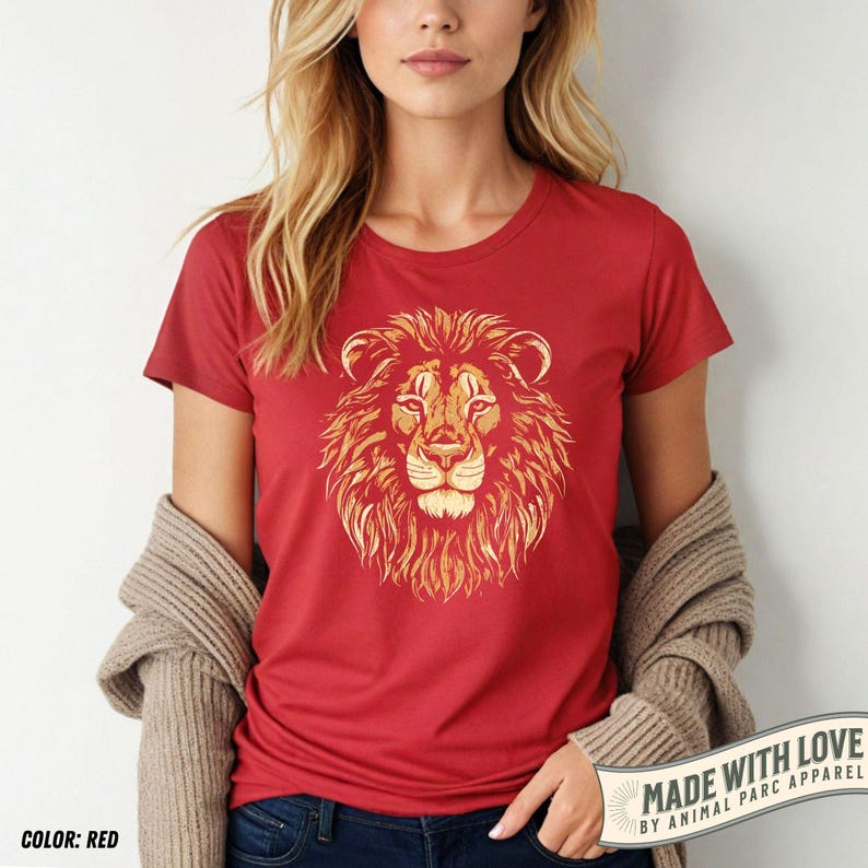 May include: Red crew neck t-shirt featuring a detailed lion's head graphic in shades of gold and brown. The text "MADE WITH LOVE BY ANIMAL PARC APPAREL" is printed on a white banner. The color of the shirt is red.