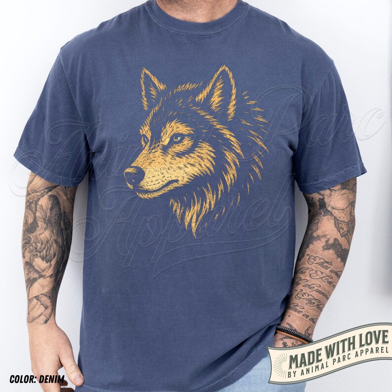 May include: Denim blue t-shirt featuring a detailed golden wolf head graphic. The shirt has short sleeves and a crew neck. The text "MADE WITH LOVE BY ANIMAL PARC APPAREL" is visible on a banner at the bottom right.