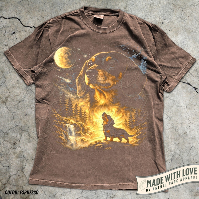 May include: Espresso-colored t-shirt featuring a detailed graphic of a dog with a forest and waterfall scene under a starry sky and moon. The shirt includes the text "MADE WITH LOVE BY ANIMAL PARC APPAREL".