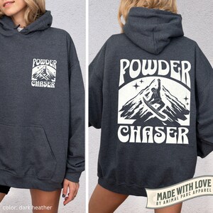 May include: Dark grey hoodie with a front pocket and hood. The front has a white graphic with "POWDER CHASER" and a mountain scene. The back shows a larger graphic with a snowboarder. Made with love by Animal Parc Apparel.