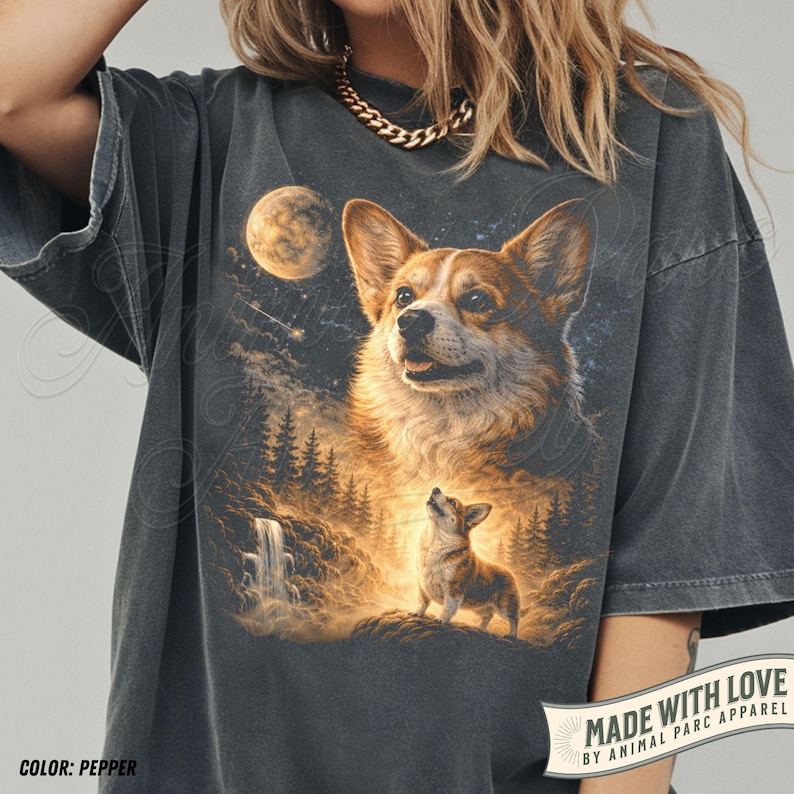 May include: Pepper-colored t-shirt featuring a detailed illustration of a Corgi dog under a full moon and starry sky. The design includes a waterfall and forest scene. The text "MADE WITH LOVE BY ANIMAL PARC APPAREL" is printed on the bottom right.