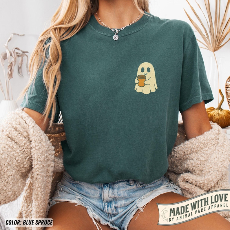 May include: Blue spruce t-shirt featuring a cartoon ghost holding a coffee cup. The ghost is beige with a smiling face, and the coffee cup is brown. The shirt has a relaxed fit and short sleeves. The text "MADE WITH LOVE BY ANIMAL PARC APPAREL" is visible.