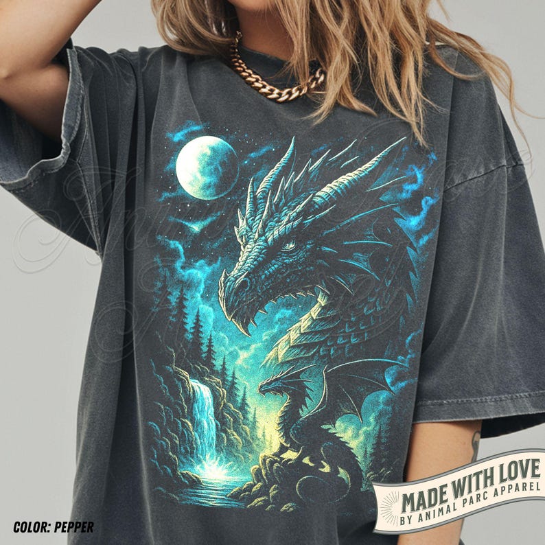 May include: Pepper-colored t-shirt featuring a detailed dragon illustration with a waterfall, moon, and forest scene. The dragon is depicted in shades of blue and teal. The text "MADE WITH LOVE BY ANIMAL PARC APPAREL" is printed on the bottom right.