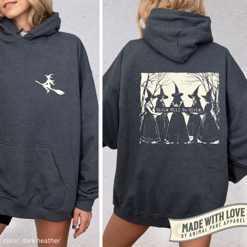 May include: Dark heather grey hoodie with a white graphic of a witch flying on a broomstick on the front and a white graphic of four witches in a forest with the text "Girls Will Be Girls." on the back.