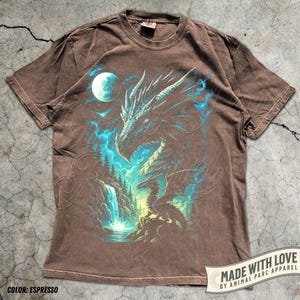 May include: Espresso-colored t-shirt featuring a detailed dragon graphic with blue and teal accents. The design includes a waterfall, moon, and forest elements. The shirt has a vintage wash and the text "MADE WITH LOVE BY ANIMAL PARC APPAREL".
