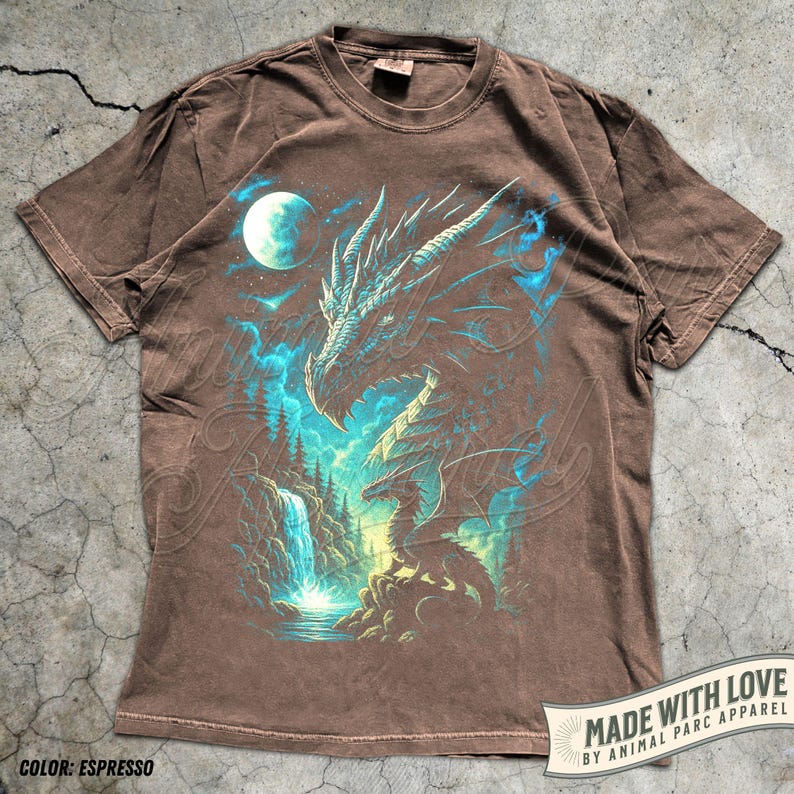 May include: Espresso-colored t-shirt featuring a detailed dragon graphic with blue and teal accents. The design includes a waterfall, moon, and forest elements. The shirt has a vintage wash and the text "MADE WITH LOVE BY ANIMAL PARC APPAREL".