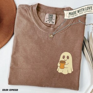 May include: Espresso-colored Comfort Colors t-shirt with a ghost graphic holding a coffee cup. The shirt has a small tag and a silver necklace. The text "MADE WITH LOVE BY ANIMAL PARC APPAREL" is visible.