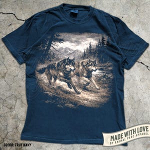 K&ouml;nnte beinhalten: Marineblaues T-Shirt mit einem sepiafarbenen Motiv von zwei W&ouml;lfen, die durch eine Waldlandschaft laufen. Das Shirt tr&auml;gt den Text "MADE WITH LOVE BY ANIMAL PARC APPAREL" und "COLOR: TRUE NAVY".