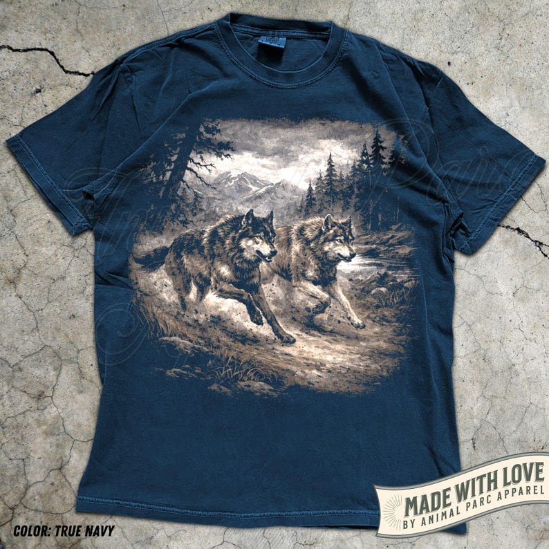 K&ouml;nnte beinhalten: Marineblaues T-Shirt mit einem sepiafarbenen Motiv von zwei W&ouml;lfen, die durch eine Waldlandschaft laufen. Das Shirt tr&auml;gt den Text "MADE WITH LOVE BY ANIMAL PARC APPAREL" und "COLOR: TRUE NAVY".