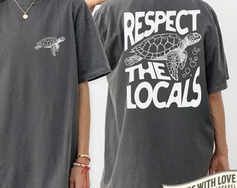 May include: Pepper-colored t-shirt featuring a white turtle graphic on the front and the text "RESPECT THE LOCALS" with a turtle illustration on the back. The shirt is a comfortable, oversized fit.
