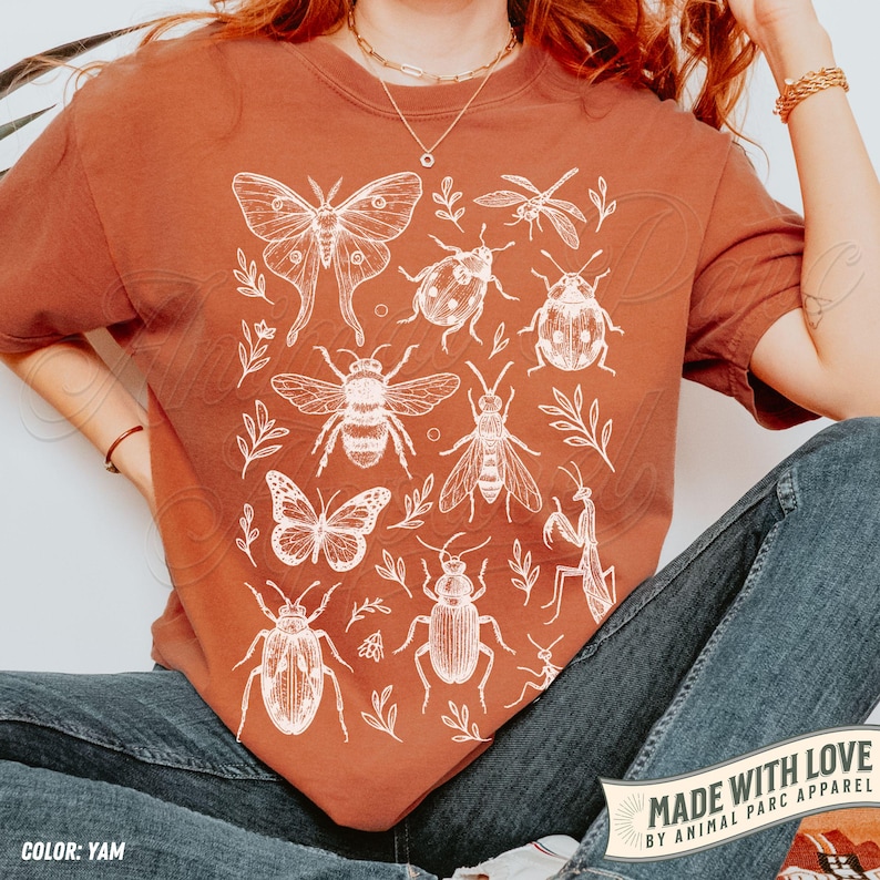 May include: A terracotta-coloured t-shirt with a white insect and plant illustration. The design includes a moth, beetles, a bee, a butterfly, and other insects. The text "MADE WITH LOVE BY ANIMAL PARC APPAREL" is visible.