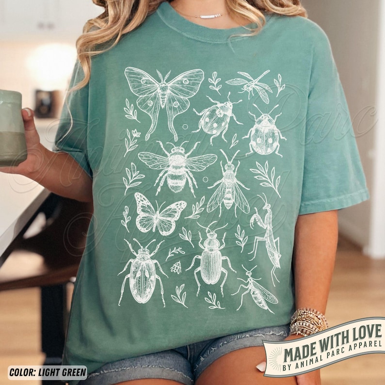 May include: Light green t-shirt with a white insect and leaf design. The design includes a butterfly, bee, dragonfly, and other insects. The text "MADE WITH LOVE BY ANIMAL PARC APPAREL" is printed on a banner.