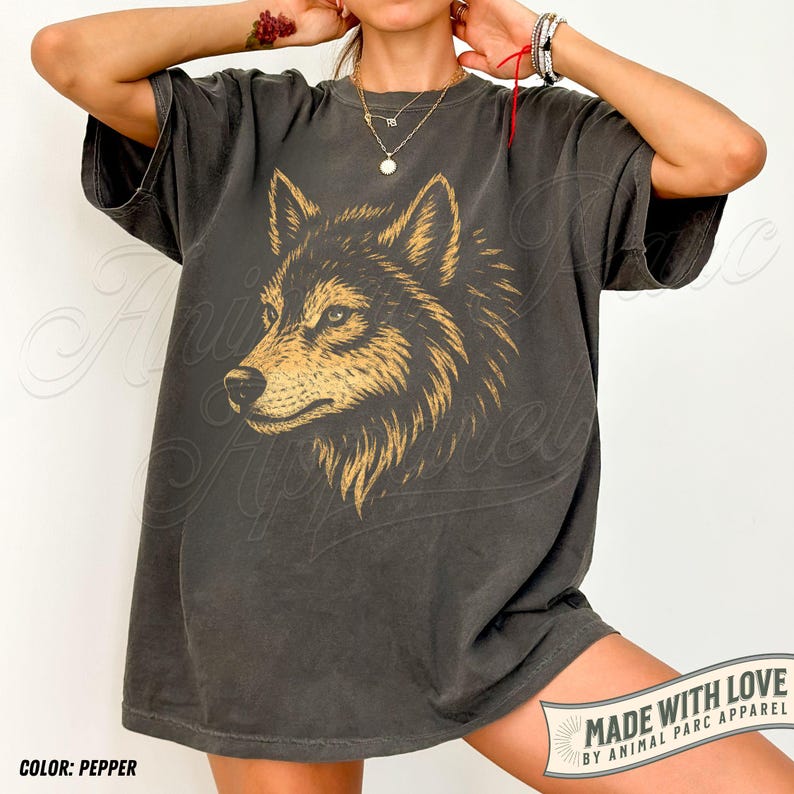 May include: Pepper-colored t-shirt featuring a detailed golden wolf graphic. The shirt has a relaxed fit and short sleeves. The text "MADE WITH LOVE BY ANIMAL PARC APPAREL" is printed on a banner at the bottom.