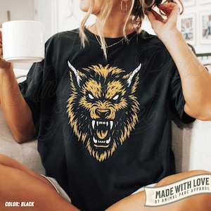May include: Black t-shirt with a yellow and white illustration of a wolf's head. The design shows a snarling wolf. The shirt includes the text "MADE WITH LOVE BY ANIMAL PARC APPAREL".