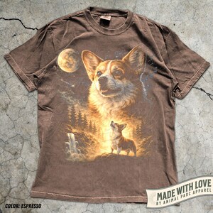 May include: Espresso-colored t-shirt featuring a detailed graphic of a Corgi dog with a celestial background, including a moon, stars, and a waterfall. The shirt has the text "MADE WITH LOVE BY ANIMAL PARC APPAREL".