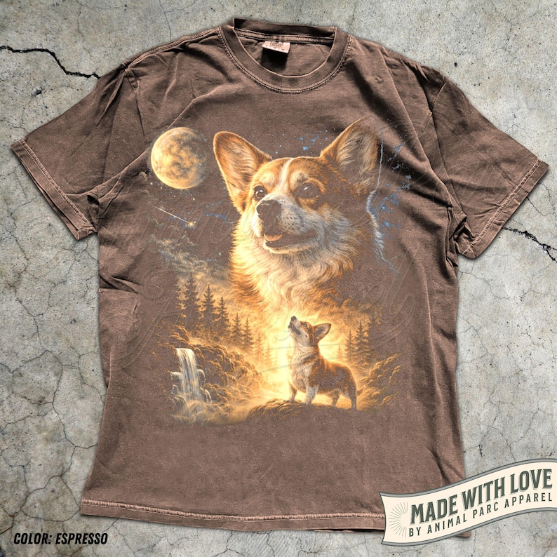May include: Espresso-colored t-shirt featuring a detailed graphic of a Corgi dog with a celestial background, including a moon, stars, and a waterfall. The shirt has the text "MADE WITH LOVE BY ANIMAL PARC APPAREL".