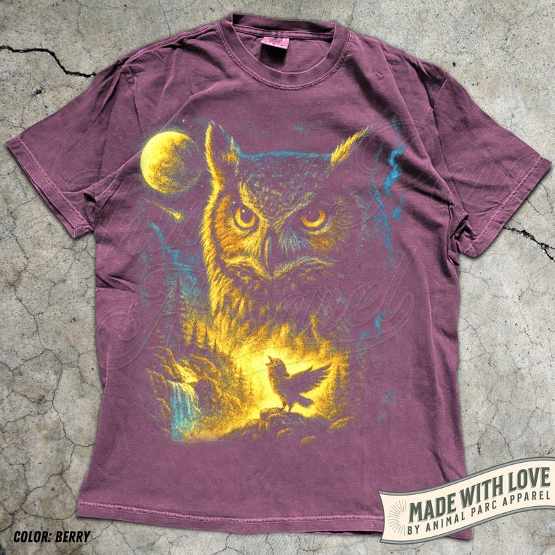 May include: Berry-coloured t-shirt with a detailed illustration of an owl, full moon, forest, and a singing bird. The design uses yellow, blue, and purple. The text "MADE WITH LOVE BY ANIMAL PARC APPAREL" is printed on the bottom right.