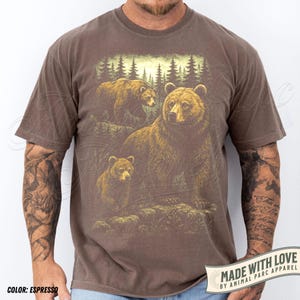 May include: Espresso-colored t-shirt featuring a detailed illustration of three bears in a forest setting. The design includes a large adult bear and two cubs, with a backdrop of trees. The shirt has the text "MADE WITH LOVE BY ANIMAL PARC APPAREL".