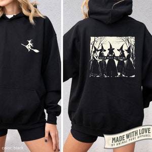 May include: Black hooded sweatshirt with a white graphic of a witch flying on a broomstick on the front and a white graphic of four witches in a forest with the text "Girls Will Be Girls." on the back.