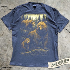 May include: Denim blue t-shirt featuring a detailed illustration of a bear family in a forest setting. The design includes a large bear with two cubs, set against a backdrop of trees. The shirt has the text "MADE WITH LOVE BY ANIMAL PARC APPAREL".