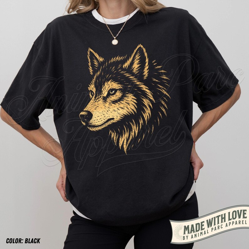 May include: Black t-shirt featuring a detailed gold and black wolf head graphic. The shirt has short sleeves and a relaxed fit. The text "MADE WITH LOVE BY ANIMAL PARC APPAREL" is printed on a banner at the bottom.