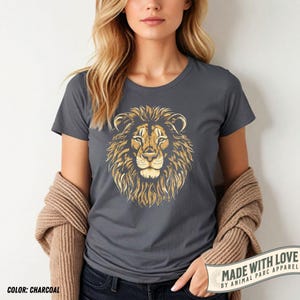 May include: Charcoal gray t-shirt featuring a detailed golden lion's head graphic. The shirt has a crew neck and short sleeves. The text "MADE WITH LOVE BY ANIMAL PARC APPAREL" is printed on a banner at the bottom right.