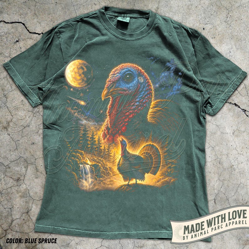 Puede incluir: Una camiseta de manga corta de color verde oscuro con un estampado gr&aacute;fico que muestra una cabeza de pavo grande en la parte superior y un pavo m&aacute;s peque&ntilde;o en un paisaje forestal con una cascada y una luna amarilla.