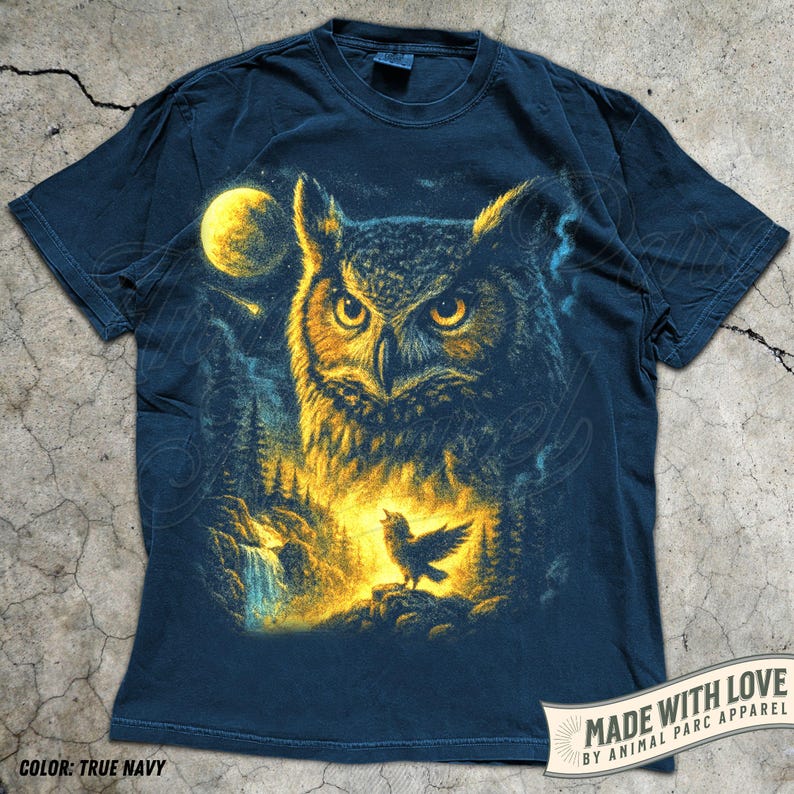 May include: True navy blue t-shirt with a detailed illustration of an owl, a full moon, and a small bird. The design includes a forest scene with a waterfall. The text "MADE WITH LOVE" is visible.