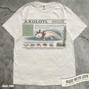 May include: Ivory t-shirt with an axolotl graphic and scientific information. The design includes the axolotl's average size, weight, habitat, and food sources. The shirt also has the text "MADE WITH LOVE BY ANIMAL PARC APPAREL."