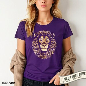 May include: Purple t-shirt featuring a detailed golden lion's head graphic. The design showcases the lion's mane, face, and eyes. The shirt is a solid purple color. The text "MADE WITH LOVE BY ANIMAL PARC APPAREL" is visible on the bottom right.