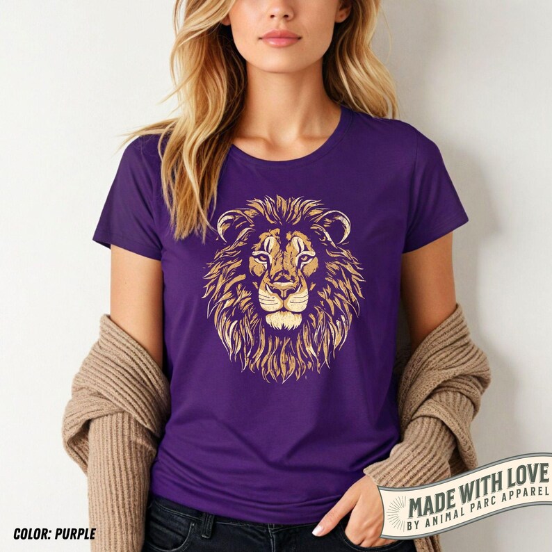 May include: Purple t-shirt featuring a detailed golden lion's head graphic. The design showcases the lion's mane, face, and eyes. The shirt is a solid purple color. The text "MADE WITH LOVE BY ANIMAL PARC APPAREL" is visible on the bottom right.