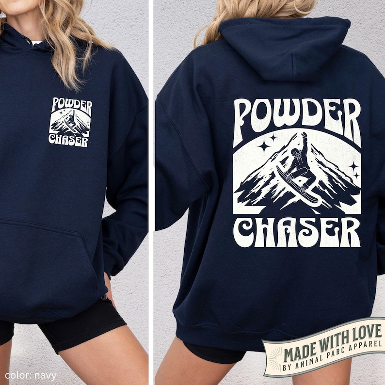 May include: Navy blue hoodie featuring a white graphic on the front and back. The front graphic reads "POWDER CHASER" with a mountain and skier design. The back graphic is larger and features the same design. Made with love by Animal Parc Apparel.