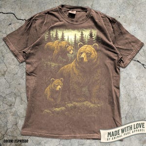 May include: Espresso-colored t-shirt featuring a detailed illustration of three brown bears in a forest setting. The design includes a large bear with two cubs, set against a backdrop of trees. The shirt has a crew neck and short sleeves. The text "MADE WITH LOVE BY ANIMAL PARC APPAREL" is also visible.