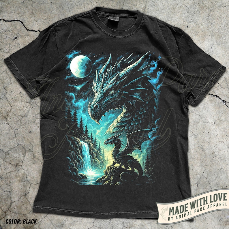 May include: Black t-shirt featuring a detailed dragon illustration. The design includes a dragon's head, a smaller dragon, a waterfall, and a full moon in a night sky. The shirt has the text "MADE WITH LOVE BY ANIMAL PARC APPAREL" and "COLOR: BLACK".