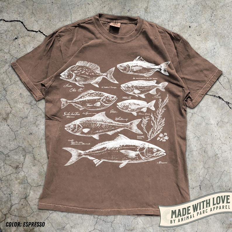 May include: Espresso-colored t-shirt featuring white illustrations of various fish species with their scientific names. The shirt includes the text "MADE WITH LOVE BY ANIMAL PARC APPAREL" on a banner.