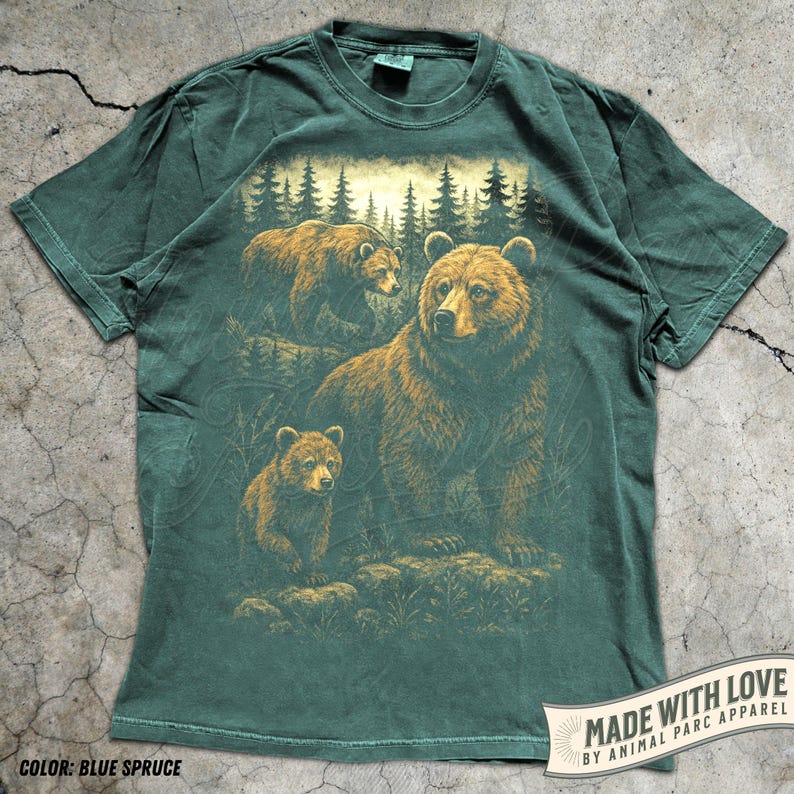 May include: Blue spruce t-shirt featuring a detailed illustration of a bear family in a forest setting. The design includes a large bear and two cubs, with a backdrop of pine trees. The shirt has a vintage look and feel.