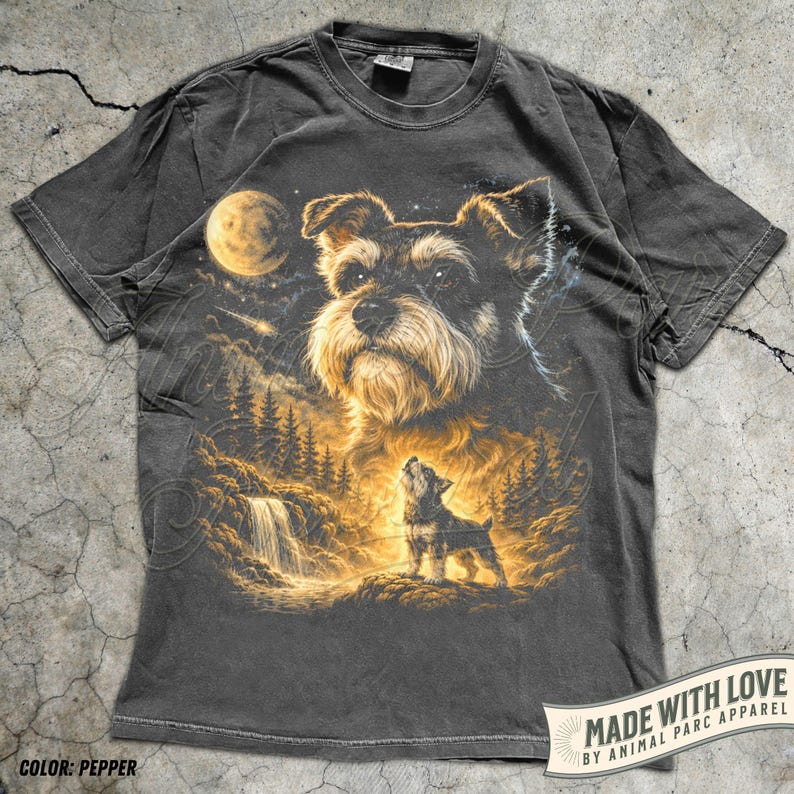 May include: Pepper-coloured t-shirt with a detailed illustration of a Schnauzer dog, a full moon, waterfall, and forest scene. The design includes a smaller Schnauzer howling at the moon. The shirt has the text "MADE WITH LOVE BY ANIMAL PARC APPAREL".