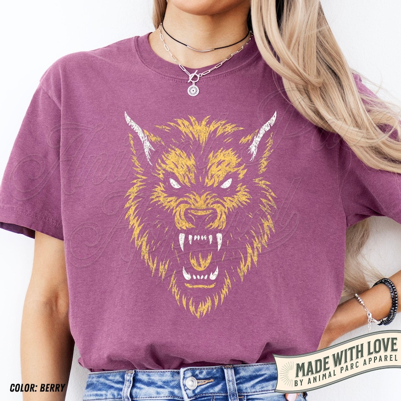 May include: Berry-coloured t-shirt with a yellow and white snarling wolf head illustration. The shirt includes the text "MADE WITH LOVE BY ANIMAL PARC APPAREL". It is a short-sleeved crew neck.