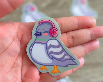 Könnte beinhalten: Ein Aufkleber mit einem Cartoon-Tauben, die einen rosa Kopfhörer mit einem Herz-Design trägt. Die Taube ist grau mit weißen Streifen und orangefarbenen Füßen. Der Aufkleber befindet sich auf einem grünen Hintergrund.