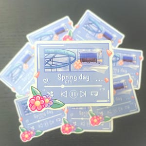 May include: A set of blue and white stickers featuring a music player design with the text "Spring day... BTS" and a floral design. The music player has a play button, a pause button, and a forward button.