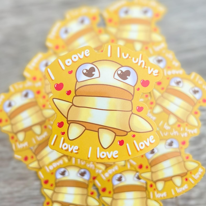K&ouml;nnte beinhalten: Ein Stapel gelber Aufkleber mit einem Comic-Charakter und dem Text "I love I love I love" und "I lu-uh-ve", der auf den Aufklebern wiederholt wird.