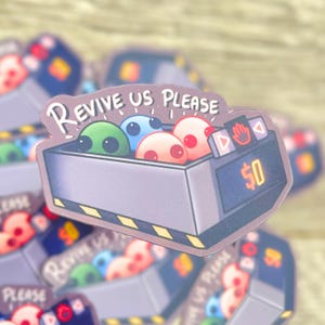K&ouml;nnte beinhalten: Ein Aufkleber mit einer Cartoon-Illustration einer Spielmaschine mit vier bunten, au&szlig;erirdisch aussehenden Figuren darin. Die Maschine hat ein Schild mit der Aufschrift "Revive Us Please" und ein Preisschild von 50 &euro;.