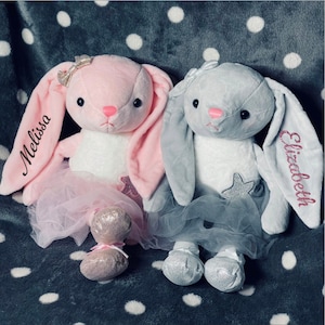 Puede incluir: Dos juguetes de peluche de conejo con tutús. El conejo rosa tiene el nombre "Melissa" bordado en su oreja y el conejo gris tiene el nombre "Elizabeth" bordado en su oreja.