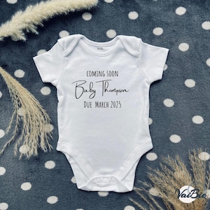 Può includere: Body bianco per neonato con testo nero che recita "Coming Soon Baby Thompson Due March 2025".